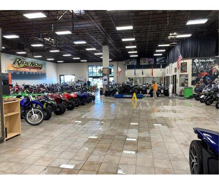 Water puddled in the middle of a motorcycle showroom. Employee extracting water.