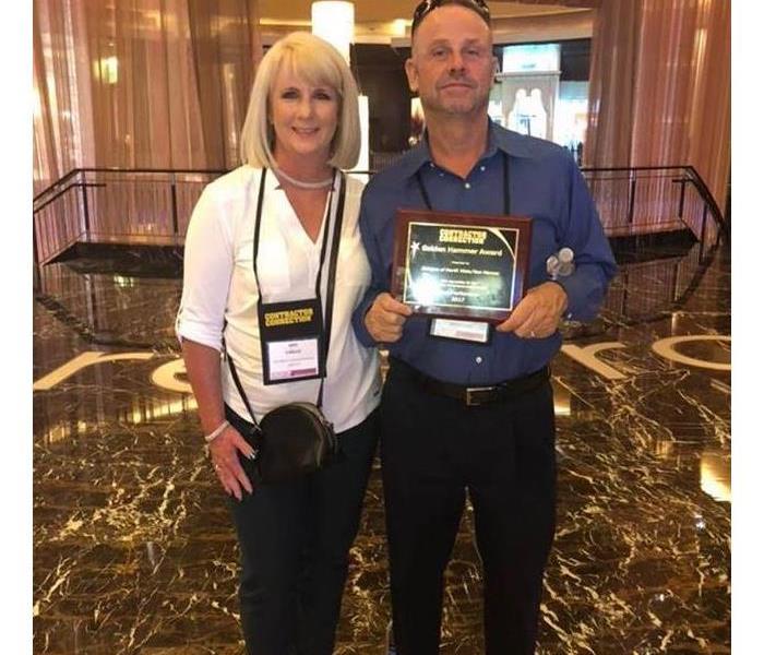 Owner and his wife standing with award.