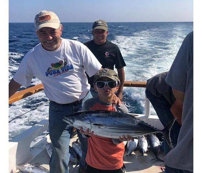 Three men holding fish on a fishing boat in the ocean.