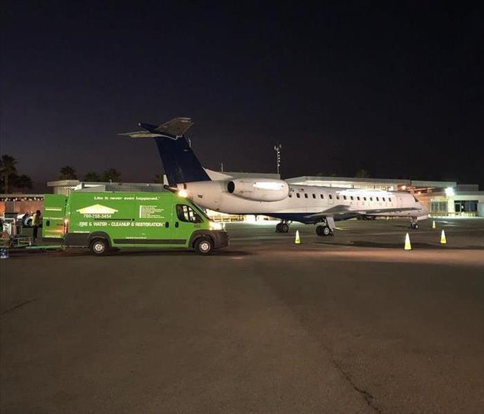 Green truck parked next to airplane on tarmac.