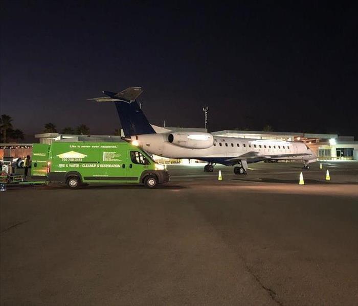 Green truck parked next to airplane on tarmac. 