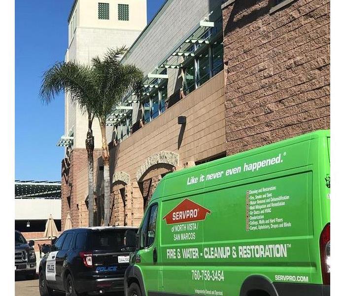 Green truck parked behind police car outside of police station.