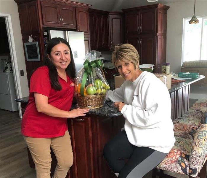 Team member smiling with homeowner and fruit gift basket in homeowners kitchen.