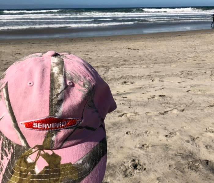 Pink SERVPRO hat in front of the beach.